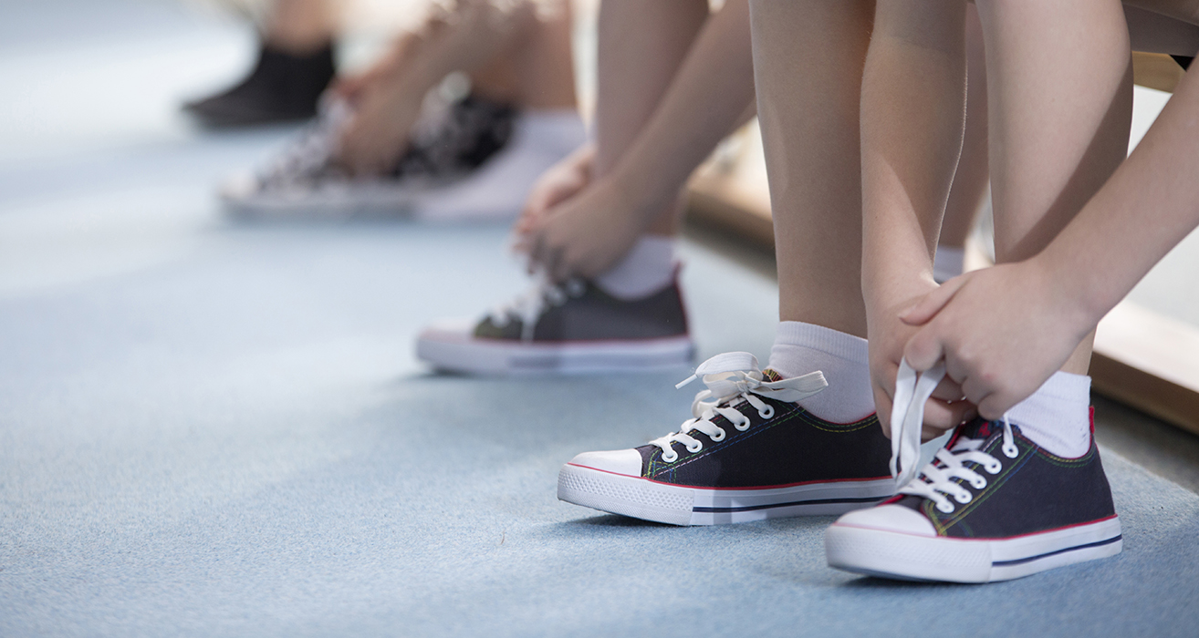 A row of students sitting on a bench tie their running shoes.