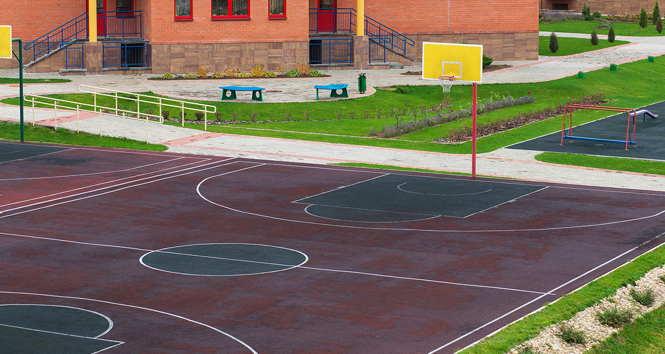 An empty basketball court sits adjacent to a school building.