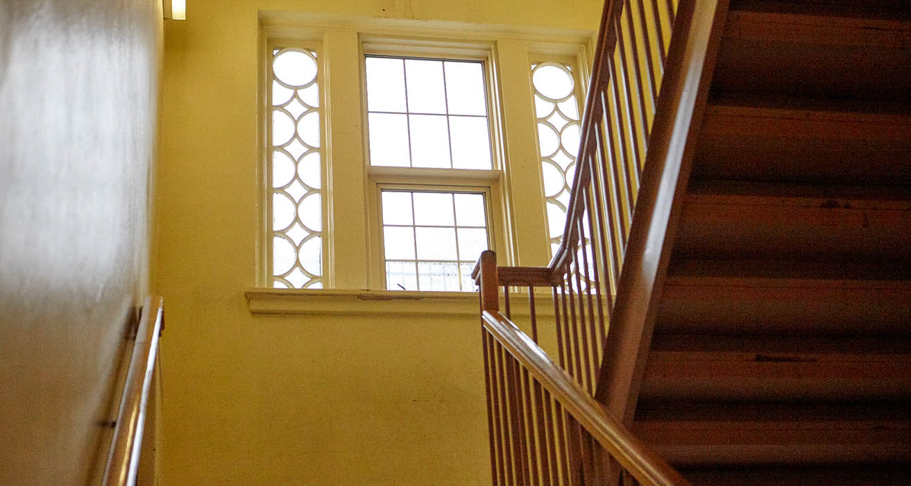 Palier d’un escalier en bois avec fenêtre ornée.